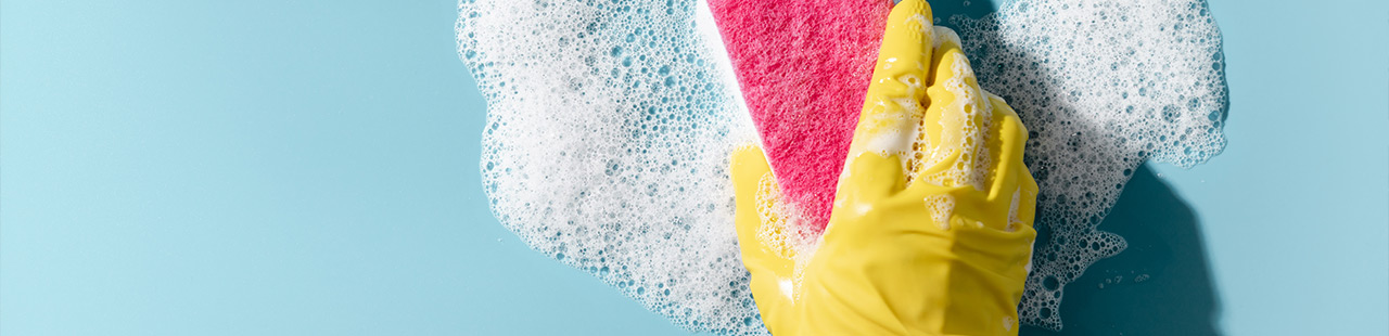 Hand mit gelbem Gummihandschuh wischt mit Schaum-Schwamm über Oberfläche