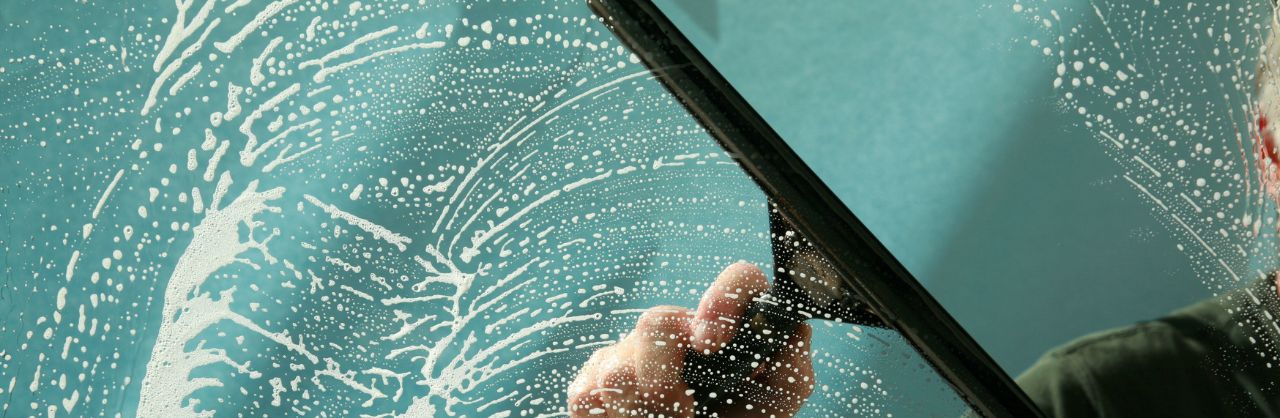 Glanzhelden – Glasreinigung – Header_03 Hand zieht Abzieher über seifige Scheibe, erzeugt streifenfreie Sauberkeit.